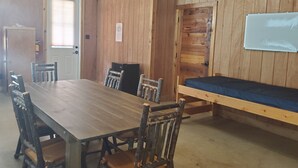 A wooden-paneled room with a large table and chairs, a bench, an exit sign, and a whiteboard. - YMCA Camp Cullen (Trinity)