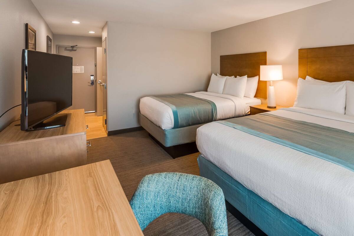 A hotel room with two beds, a TV, a desk, and a chair.