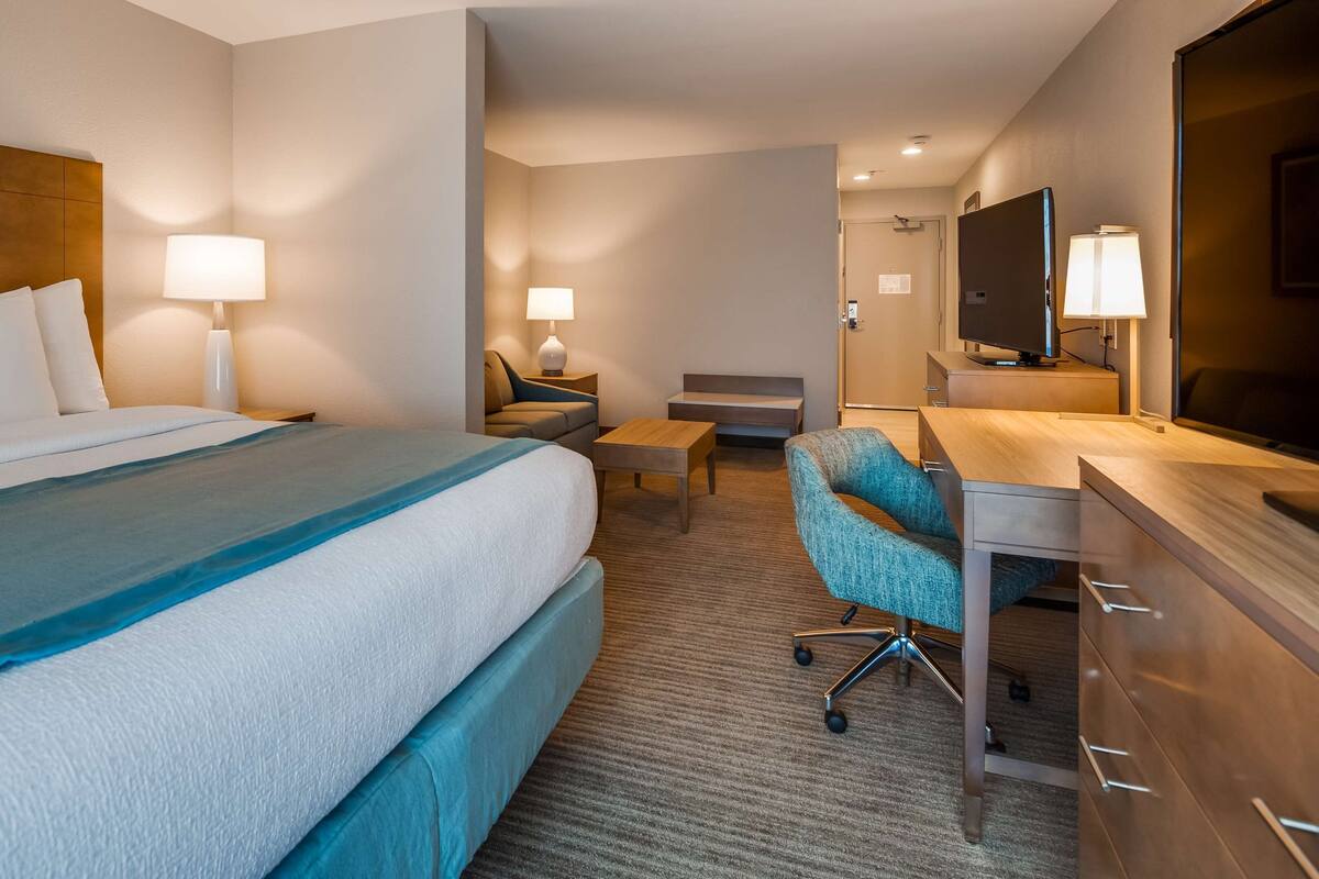 A hotel room with a large bed, a desk with a chair, a television, and a bathroom with a mirror.