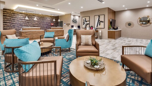 A modern hotel lobby with a reception desk, seating area with sofas and armchairs, and a patterned floor. - Best Western Plus Desoto (Olive Branch)