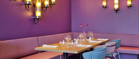 A restaurant interior with a purple wall, a wooden table set with wine glasses, and a bench.