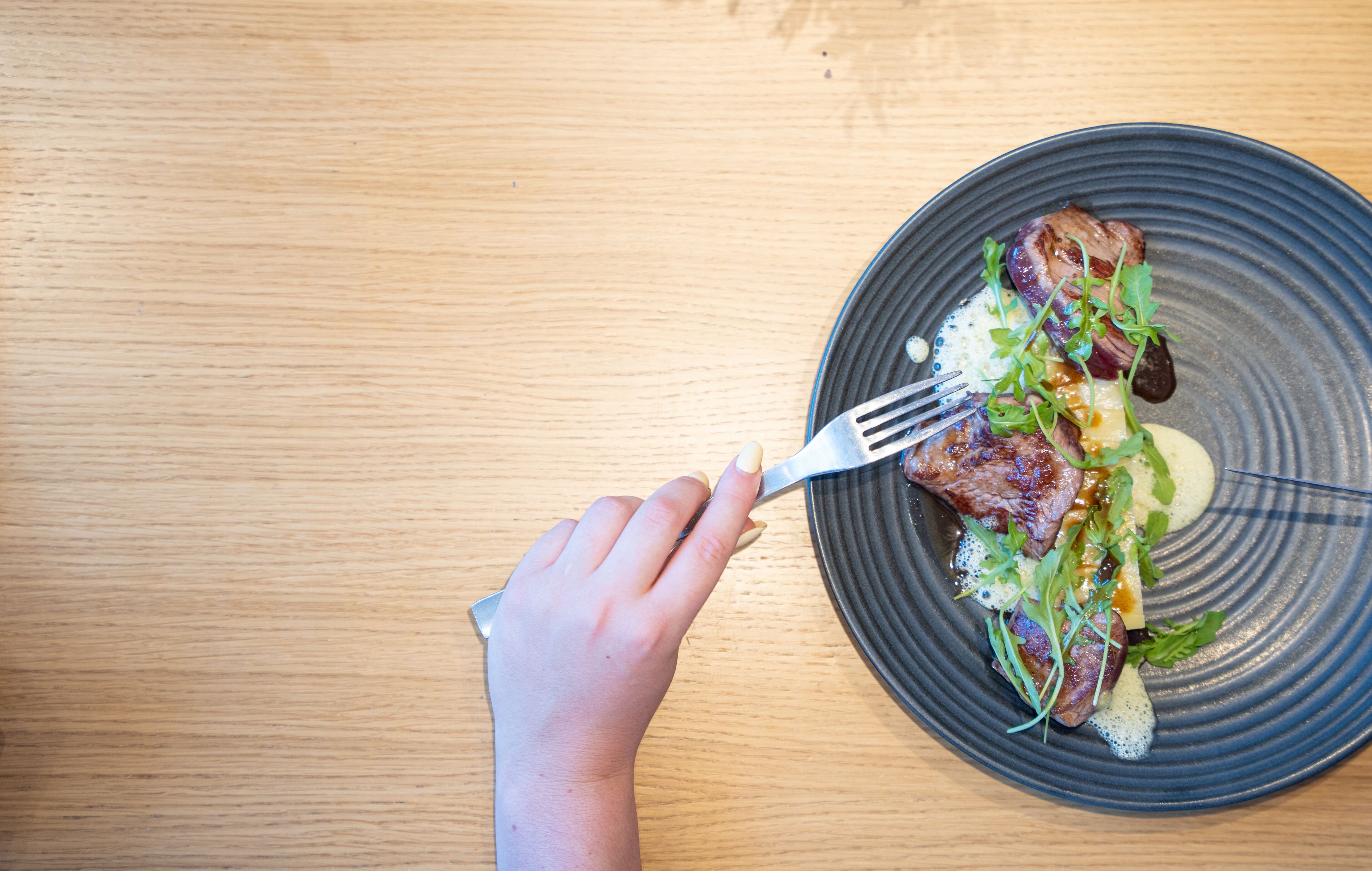 A hand holding a fork over a plate with food.