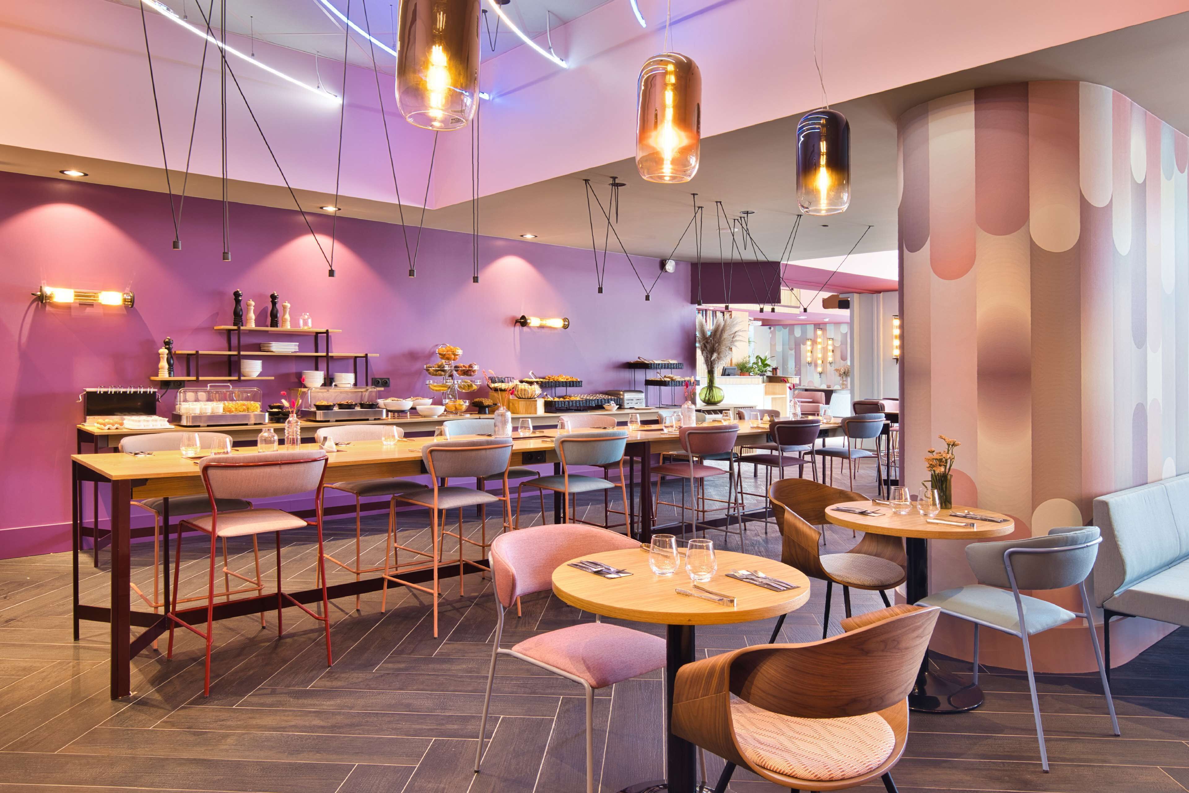 A modern restaurant interior with multiple dining tables and chairs, pendant lighting, and a bar area.