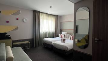 A hotel room with two beds, a desk, a chair, a mirror, and a window with curtains.