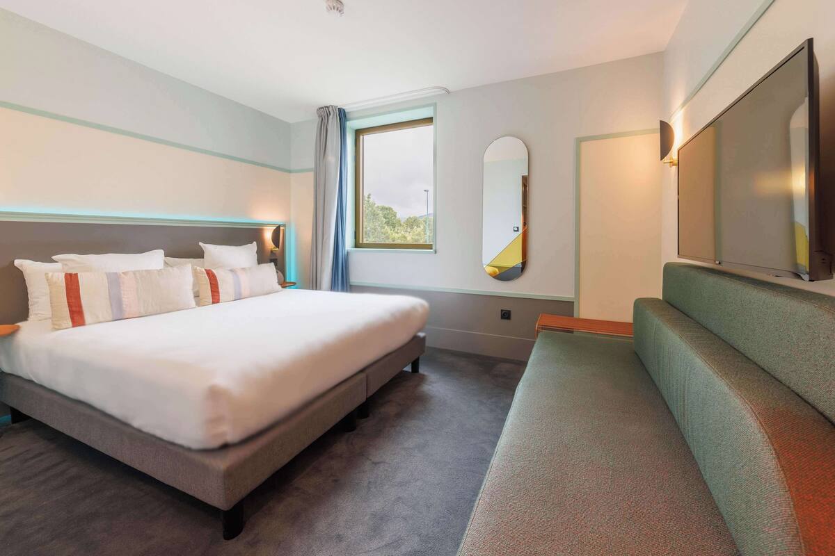 Ein Hotelzimmer mit einem Bett, einem Sofa, einem großen Spiegel und einem Fenster mit Vorhängen.