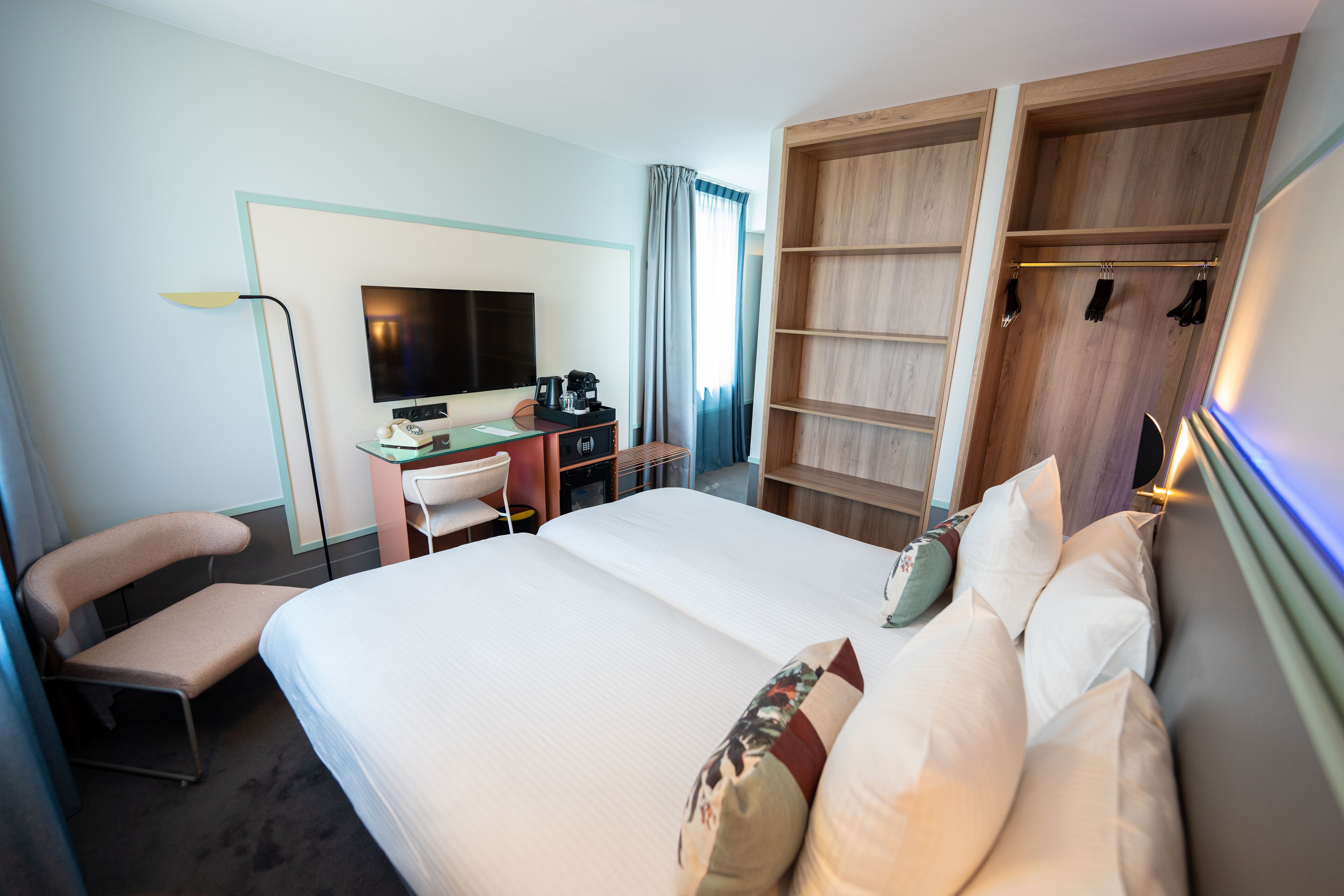 A hotel room with a bed, a desk with a computer, a TV, and a wardrobe.