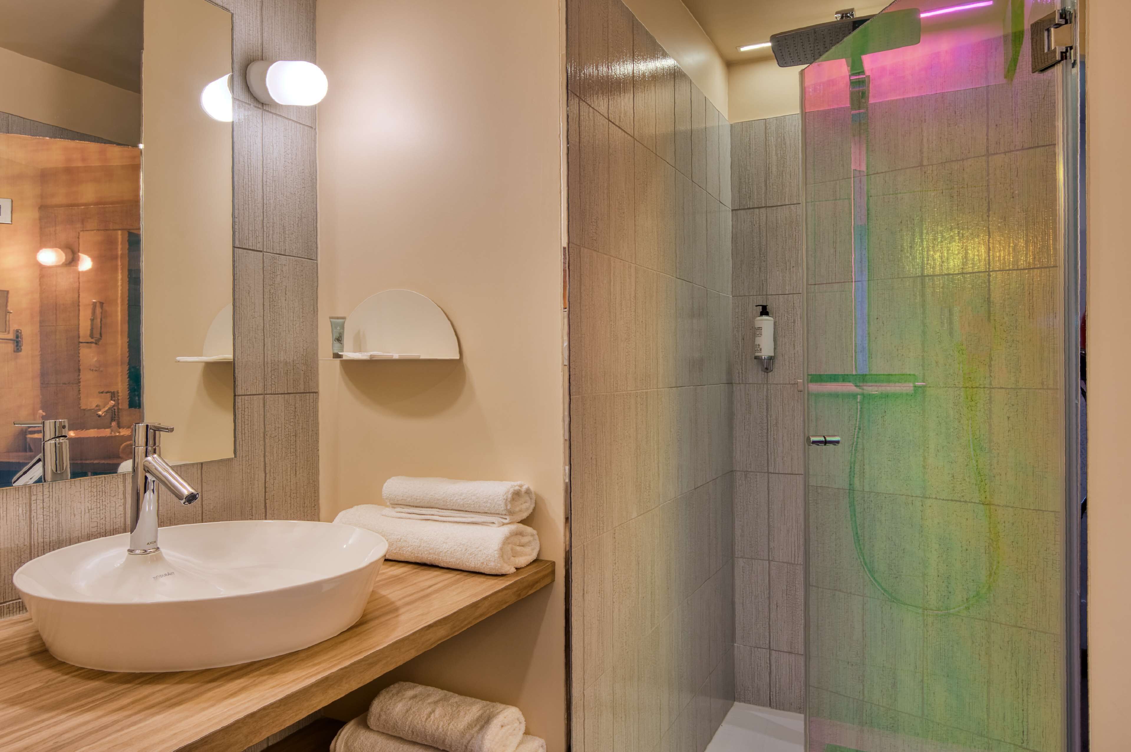 A modern bathroom with a large white sink, a mirror, and a glass-enclosed shower.
