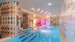 Una piscina con azulejos azules, una escalera con barandilla de metal y paredes con un diseño de baldosas en damero.
