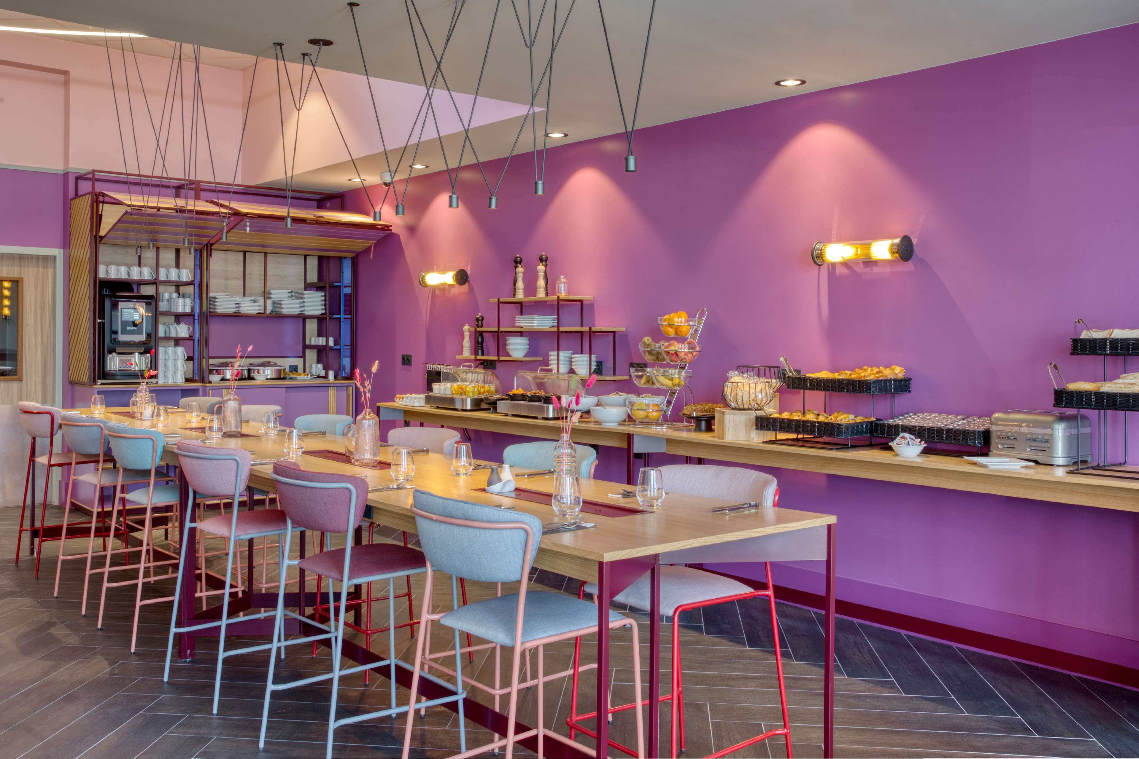 Un restaurant moderne avec des murs violets, de nombreuses tables et des chaises aux couleurs vives.