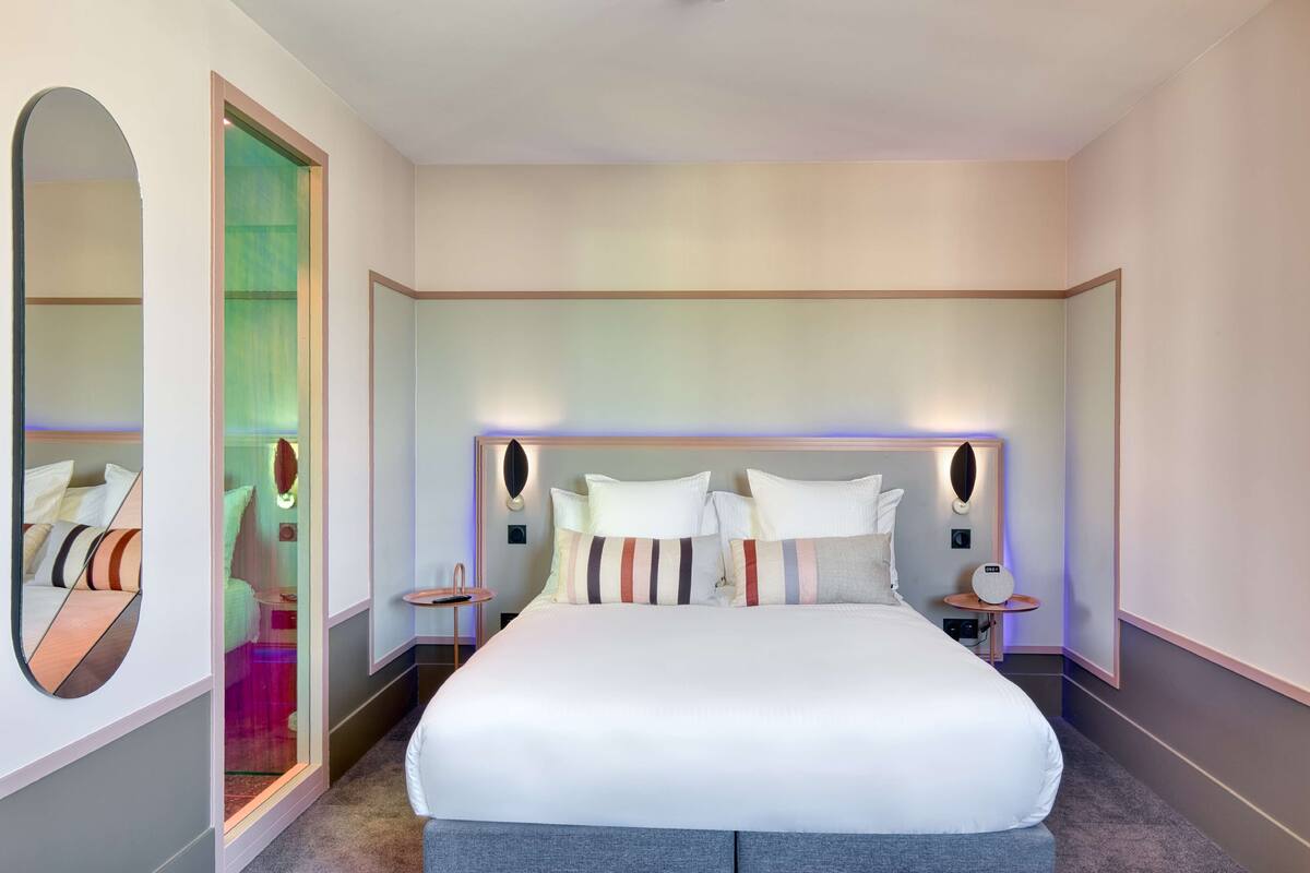 Ein modernes Hotelzimmer mit einem großen Bett, Nachttischen, einem Spiegel und Blick ins Zimmerinnere.