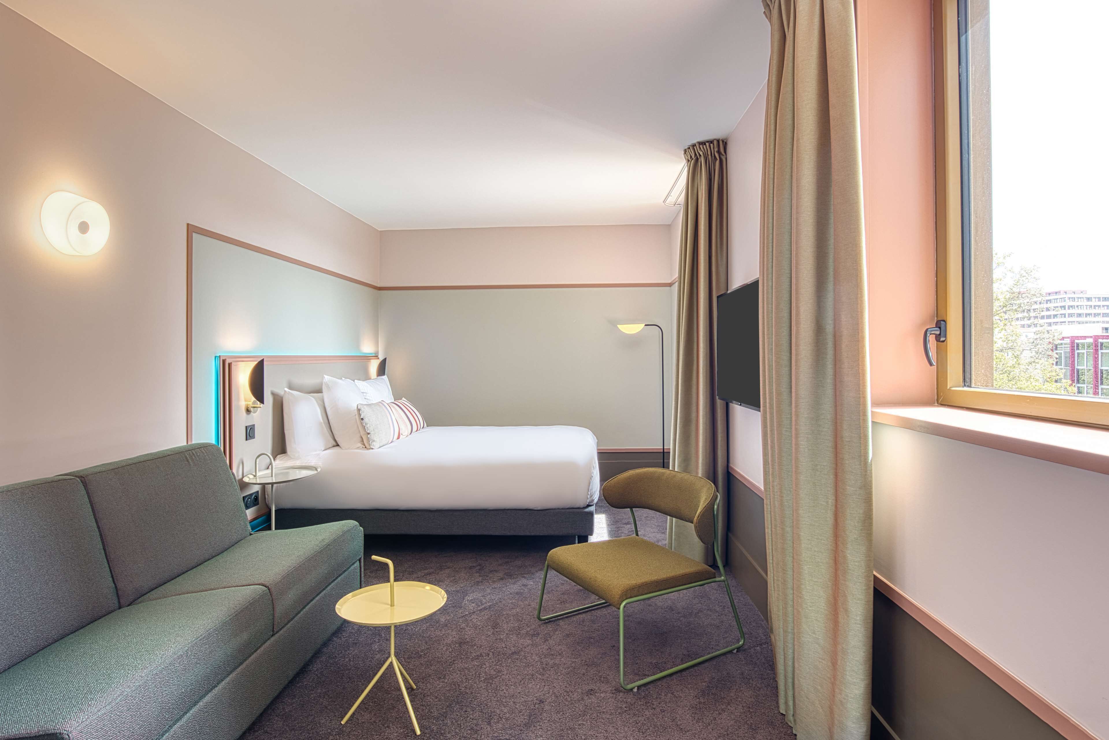 A hotel room with a bed, a sofa, a chair, a small table, and a TV.