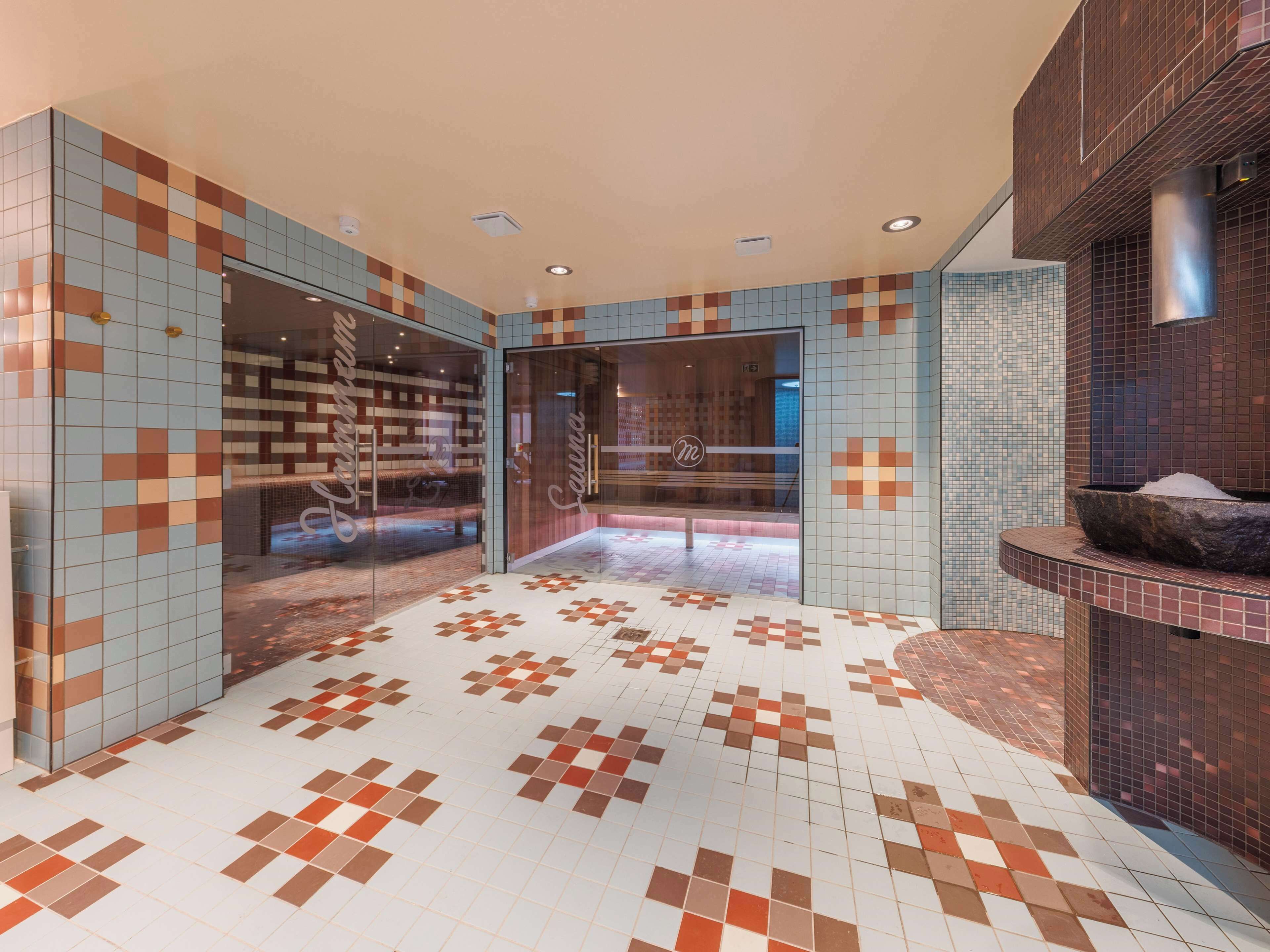 A modern lobby with patterned tile floors and walls, a reception desk, and a stone basin.
