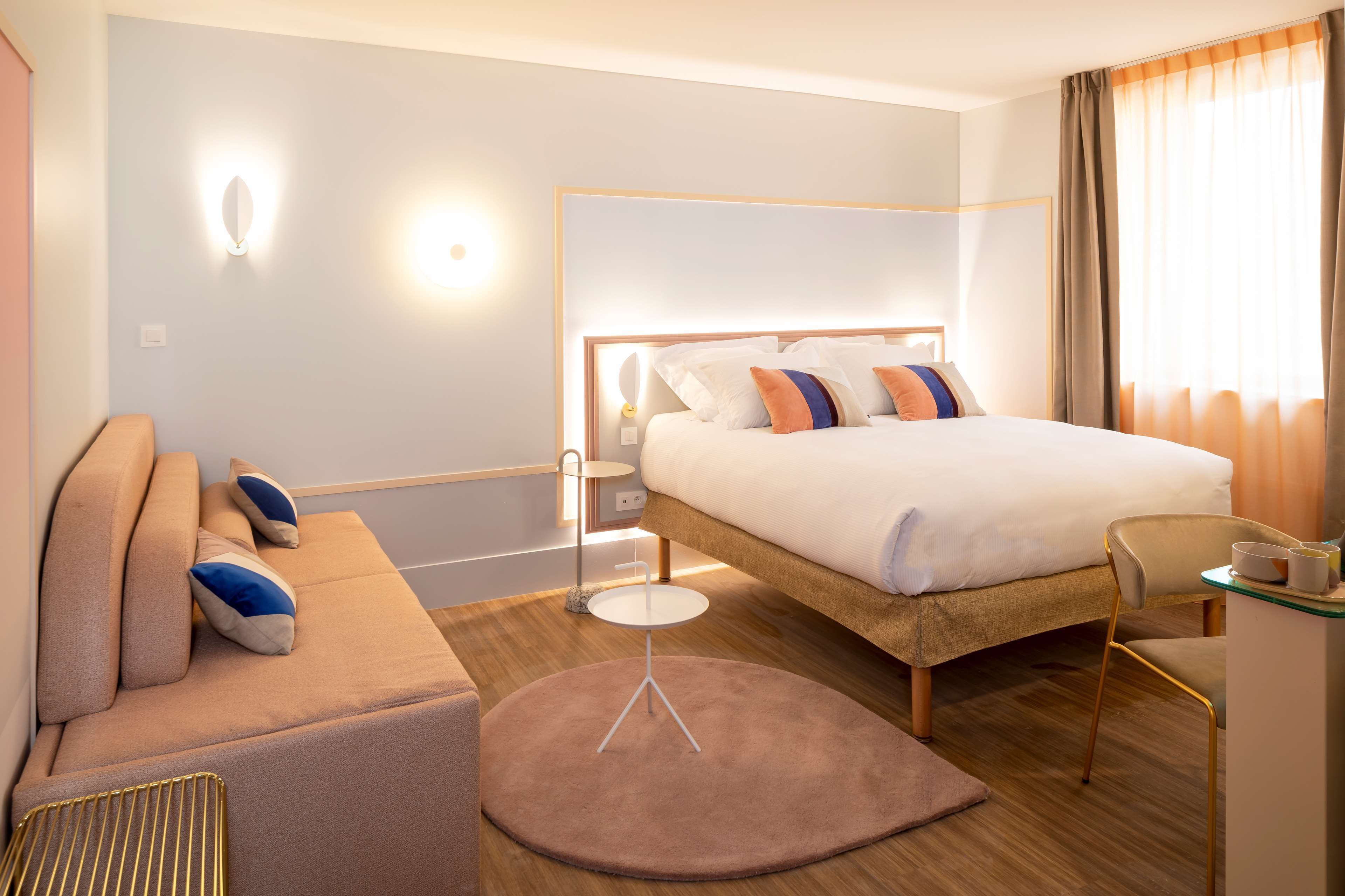 Una habitación de hotel moderna con una cama grande, un sofá, una mesita y una silla.