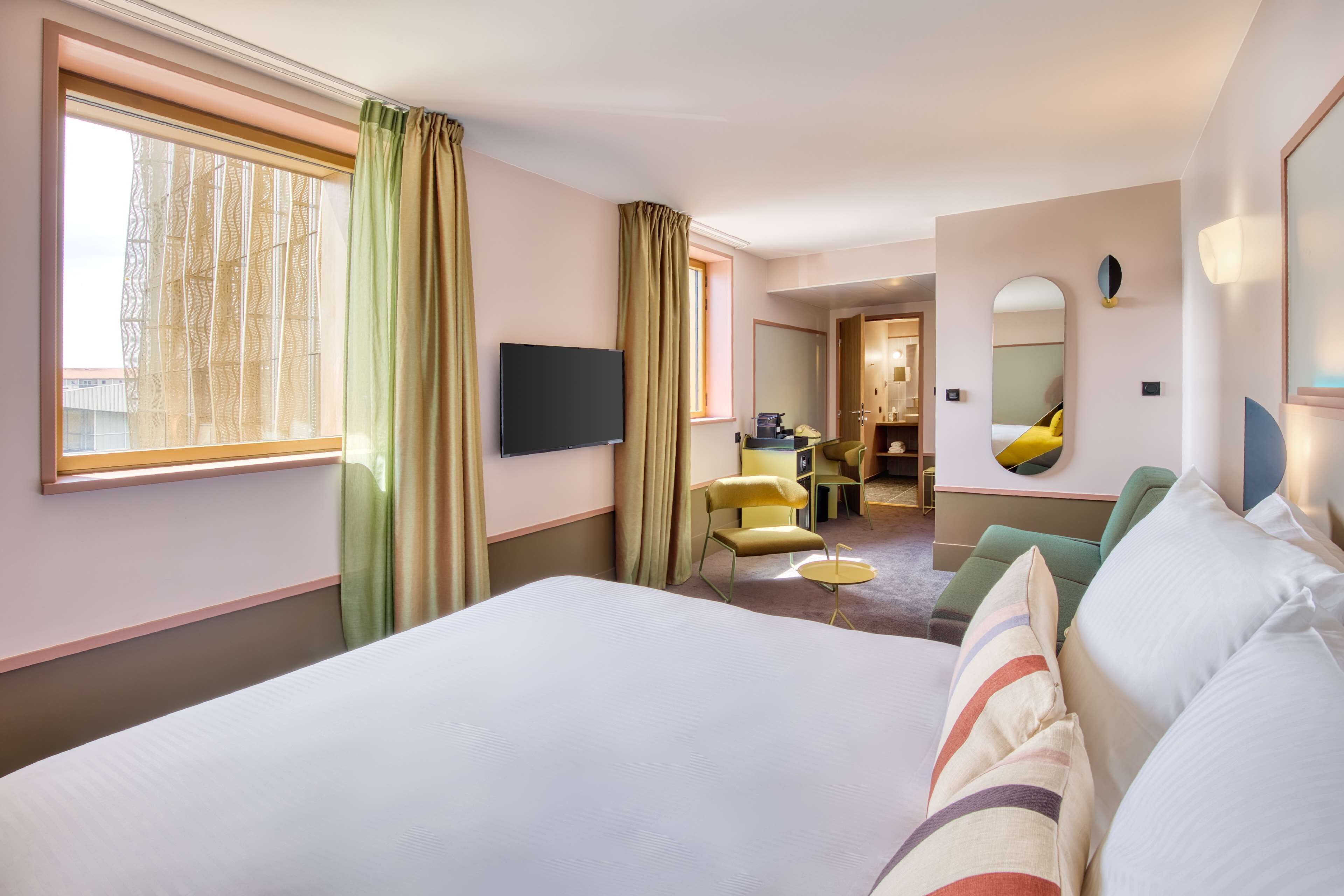 A hotel room with a large bed, a TV, a desk with a chair, and a mirror.