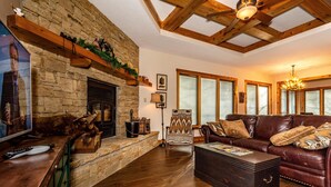 A cozy living room with a stone fireplace, wooden beams, a leather sofa, and a television. - 2BR, 2BA Log Cabin (Nashville)