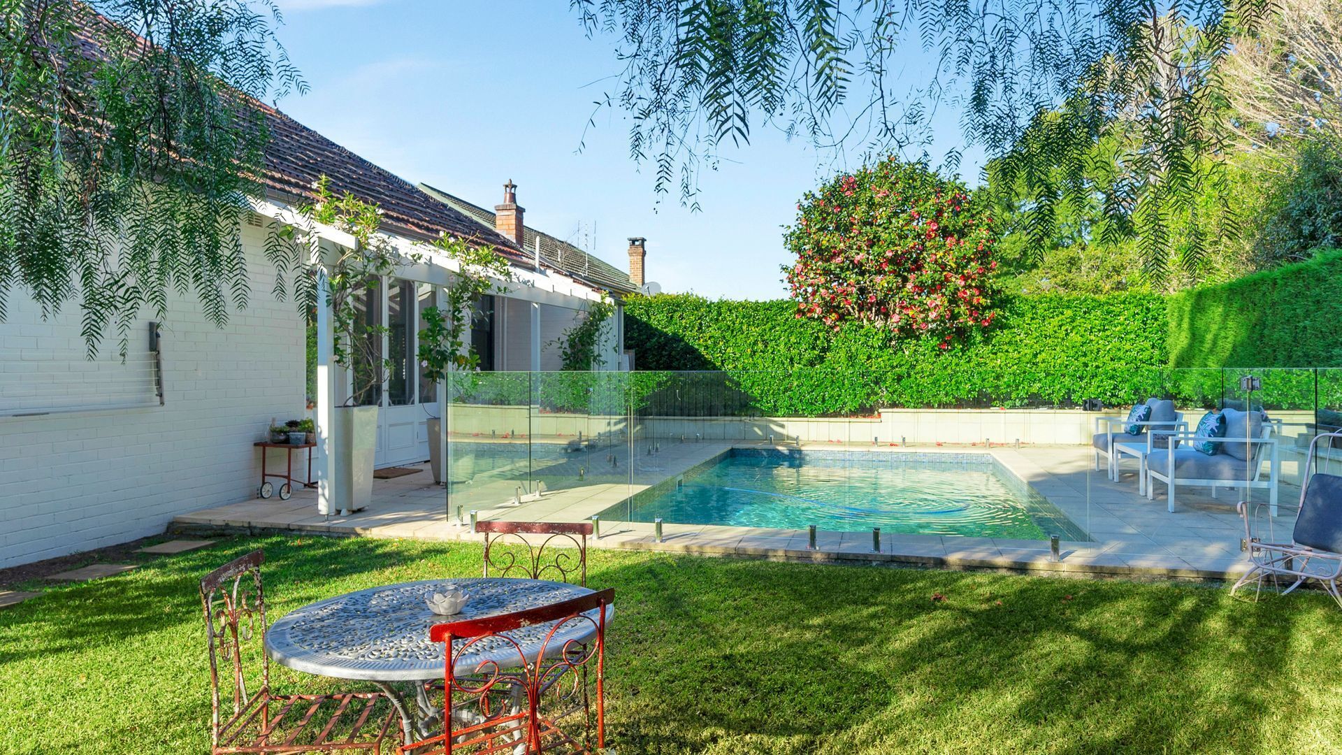 A backyard with a swimming pool, a patio table, and outdoor seating.