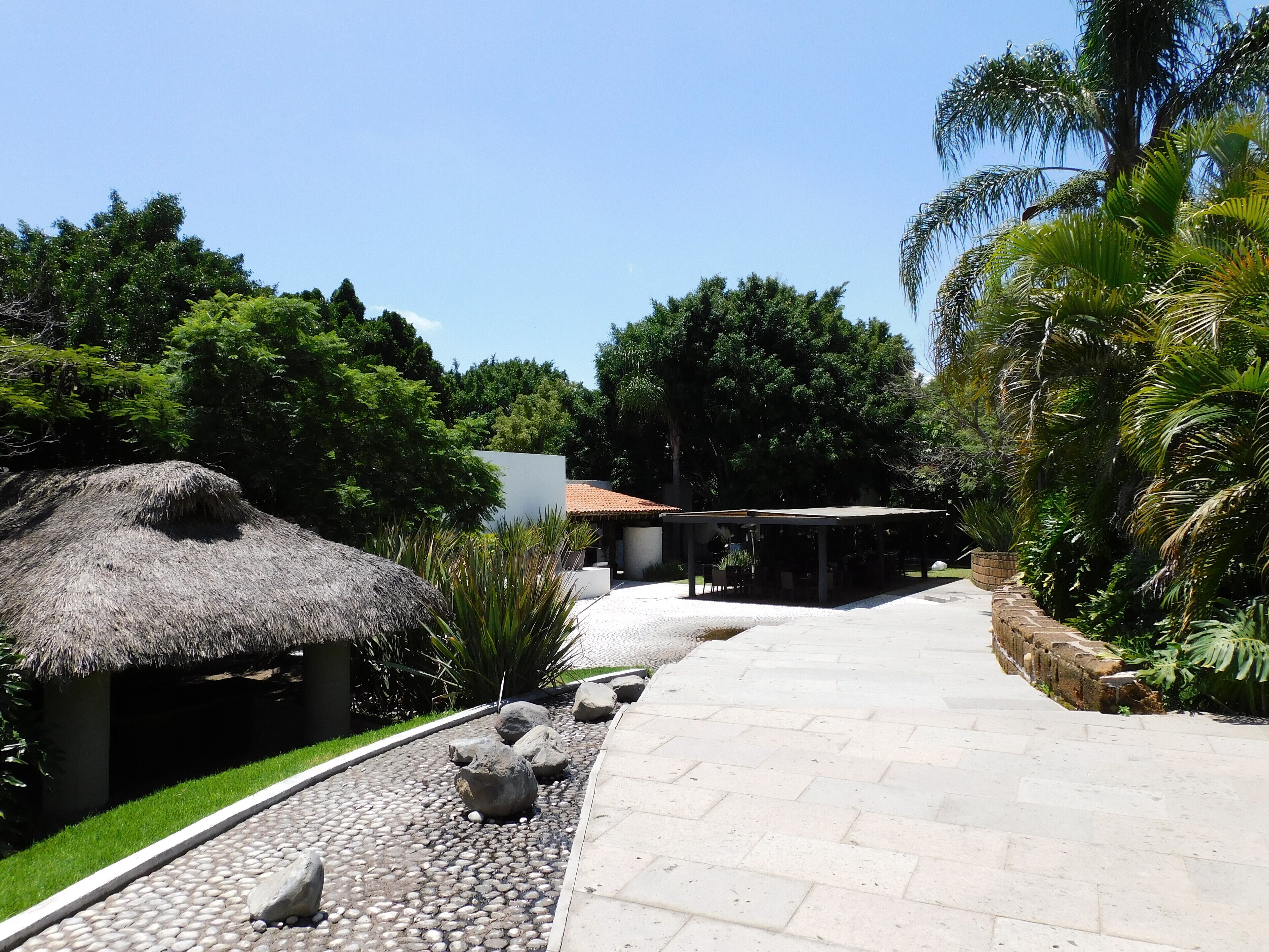 A pathway leading to a covered area with a thatched-roof structure and a building with a tiled roof.