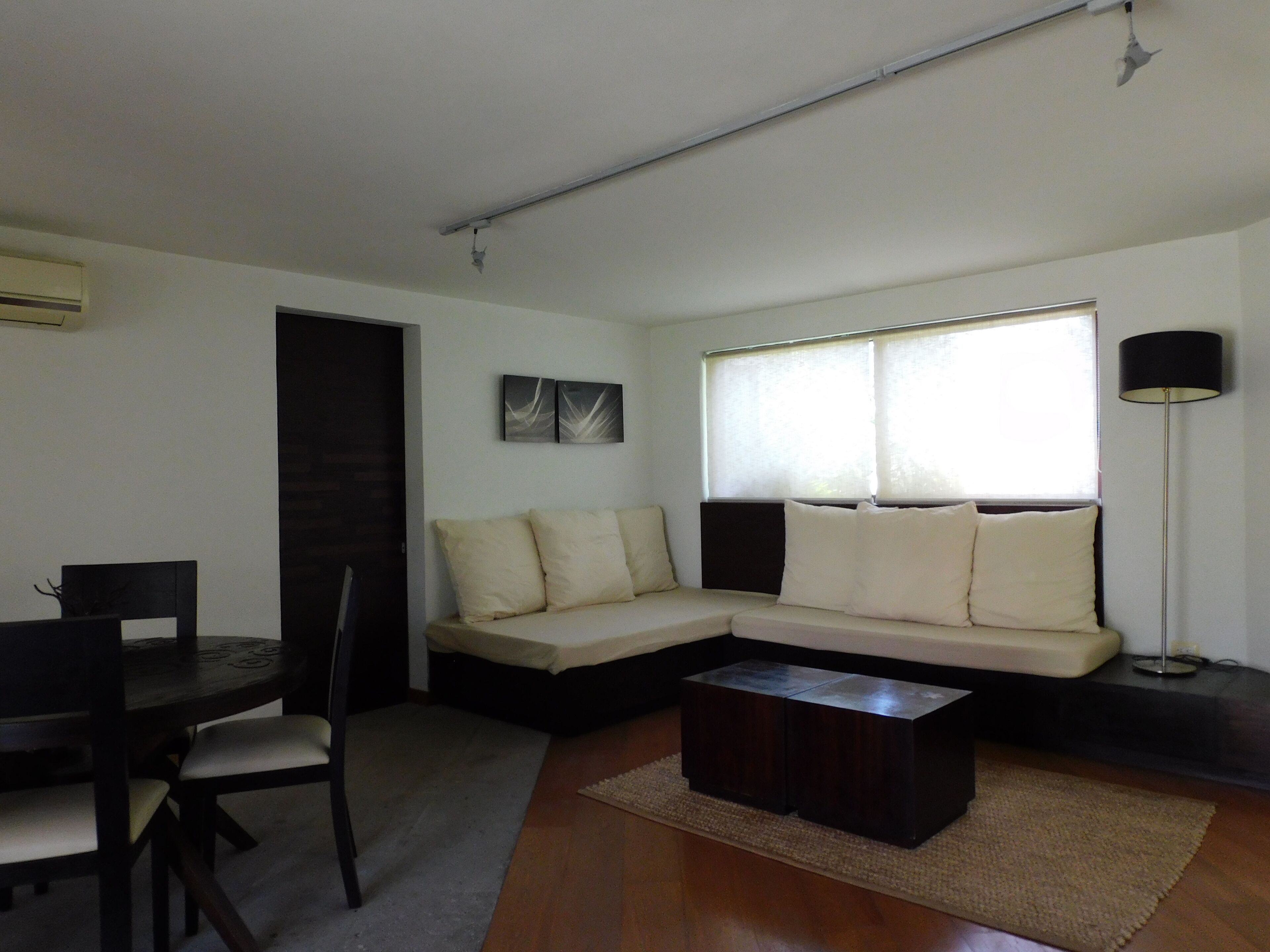 A living room with a sofa, a coffee table, a dining table with chairs, and a window with blinds.