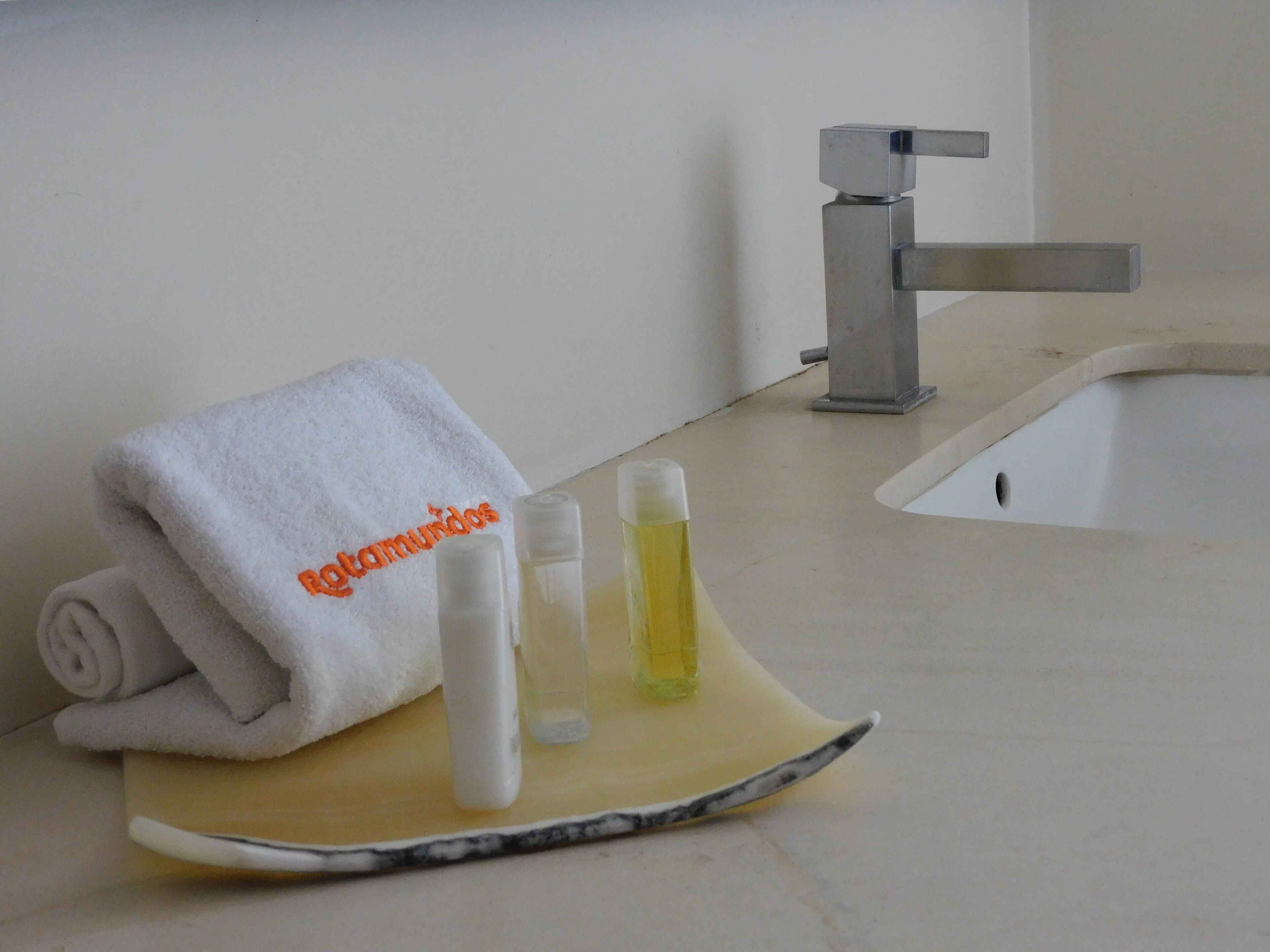 Un baño con una toalla, un dispensador de jabón y una botella de loción sobre una bandeja.