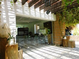 Un espacio exterior moderno con puerta de vidrio que da a una habitación, rodeado de plantas y mobiliario de madera.