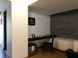 Una pequeña kitchenette con refrigerador, cafetera y una silla. Hay un cuadro en la pared y un panel de pared texturizado.