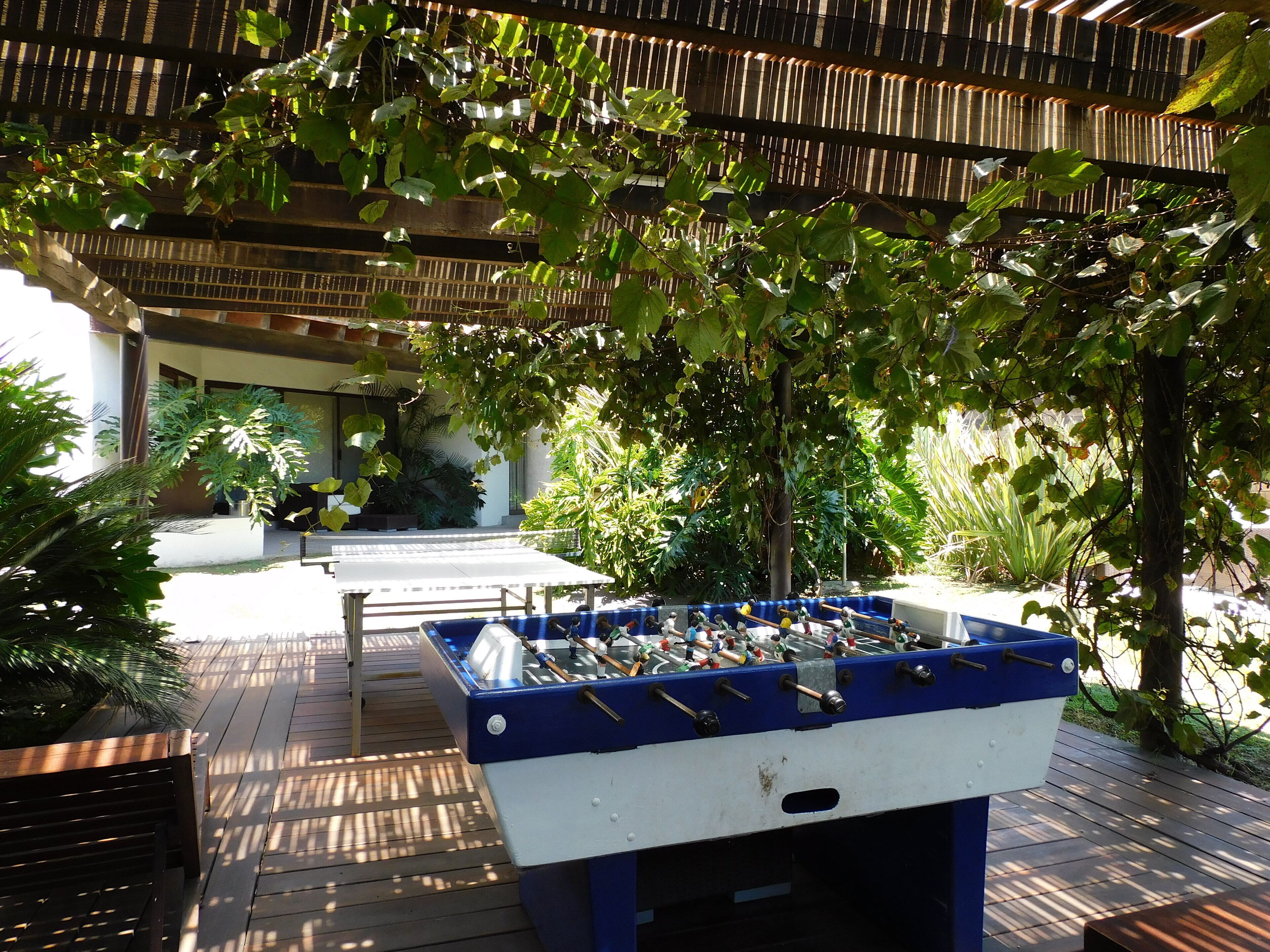 An outdoor area with a foosball table, wooden deck, and surrounding greenery.