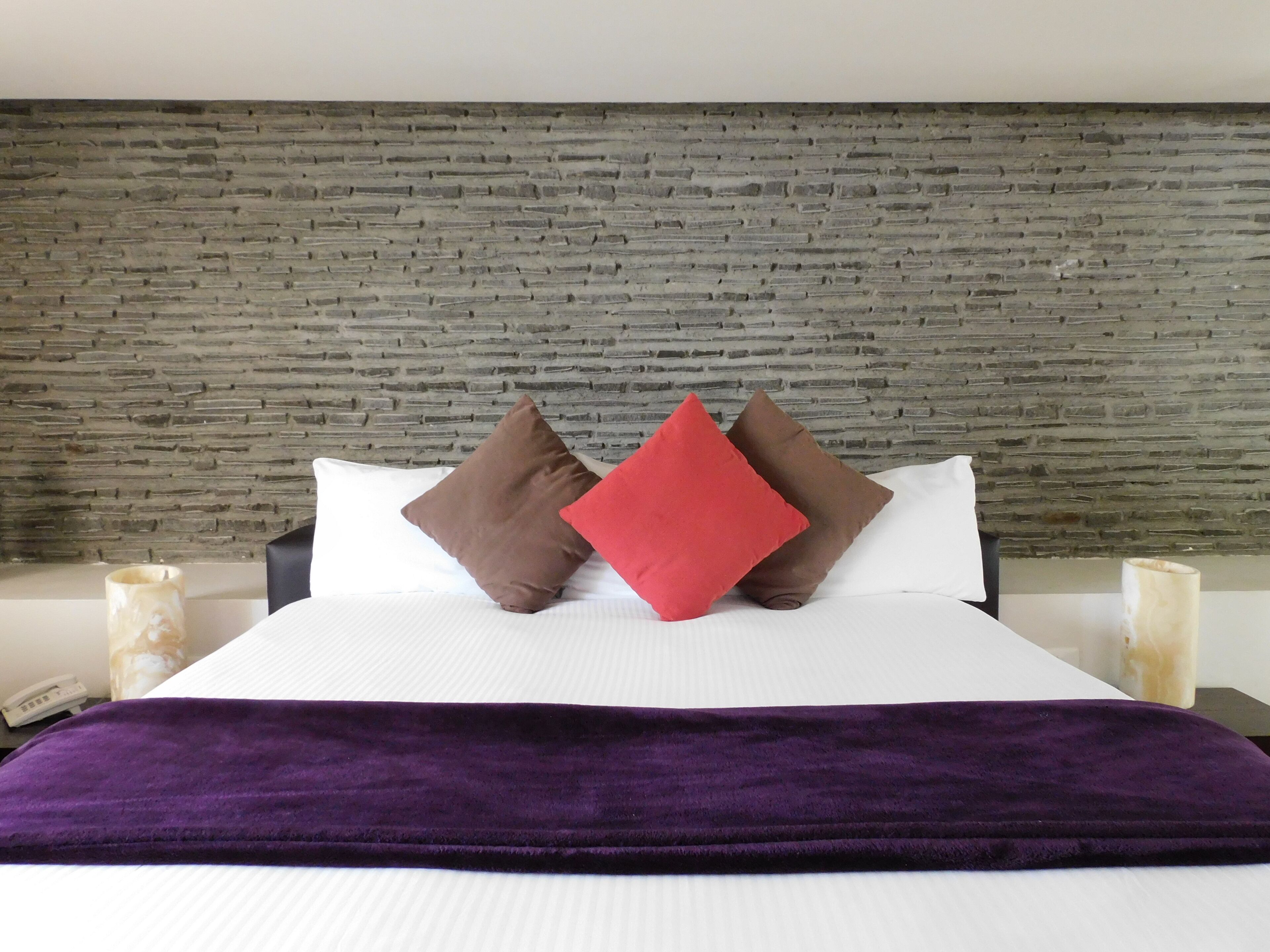 A bed with a brick-patterned headboard, two pillows, a purple throw blanket, and bedside tables with candles.