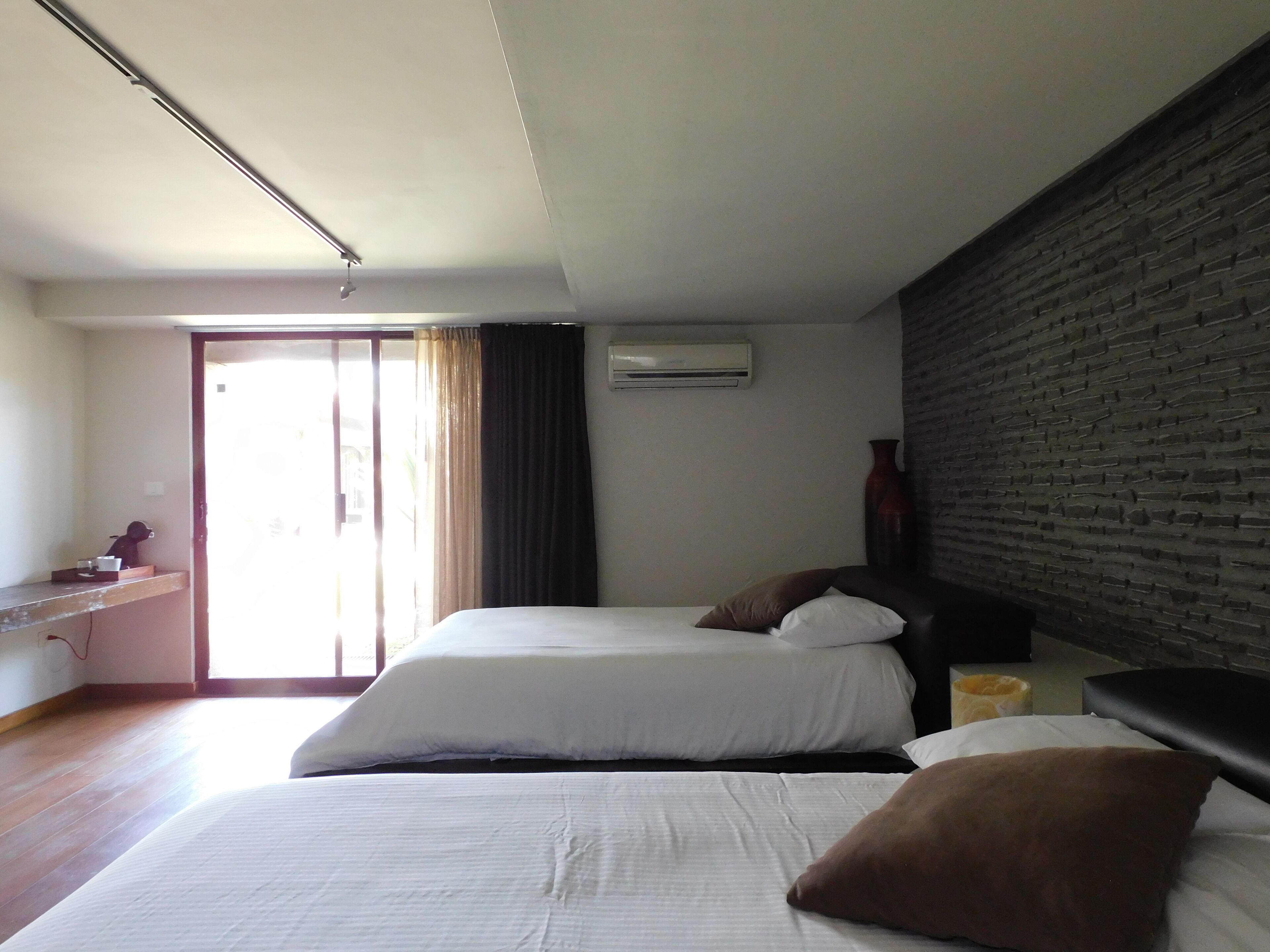 Una habitación de hotel con dos camas, un escritorio y un ventanal con cortinas.