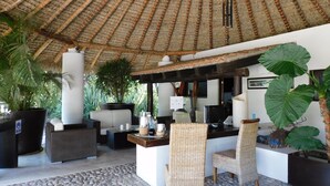 A covered outdoor seating area with wicker furniture, a large potted plant, and a stone-tiled floor. - Hotel & Spa Luna Canela Boutique (Atlixco)