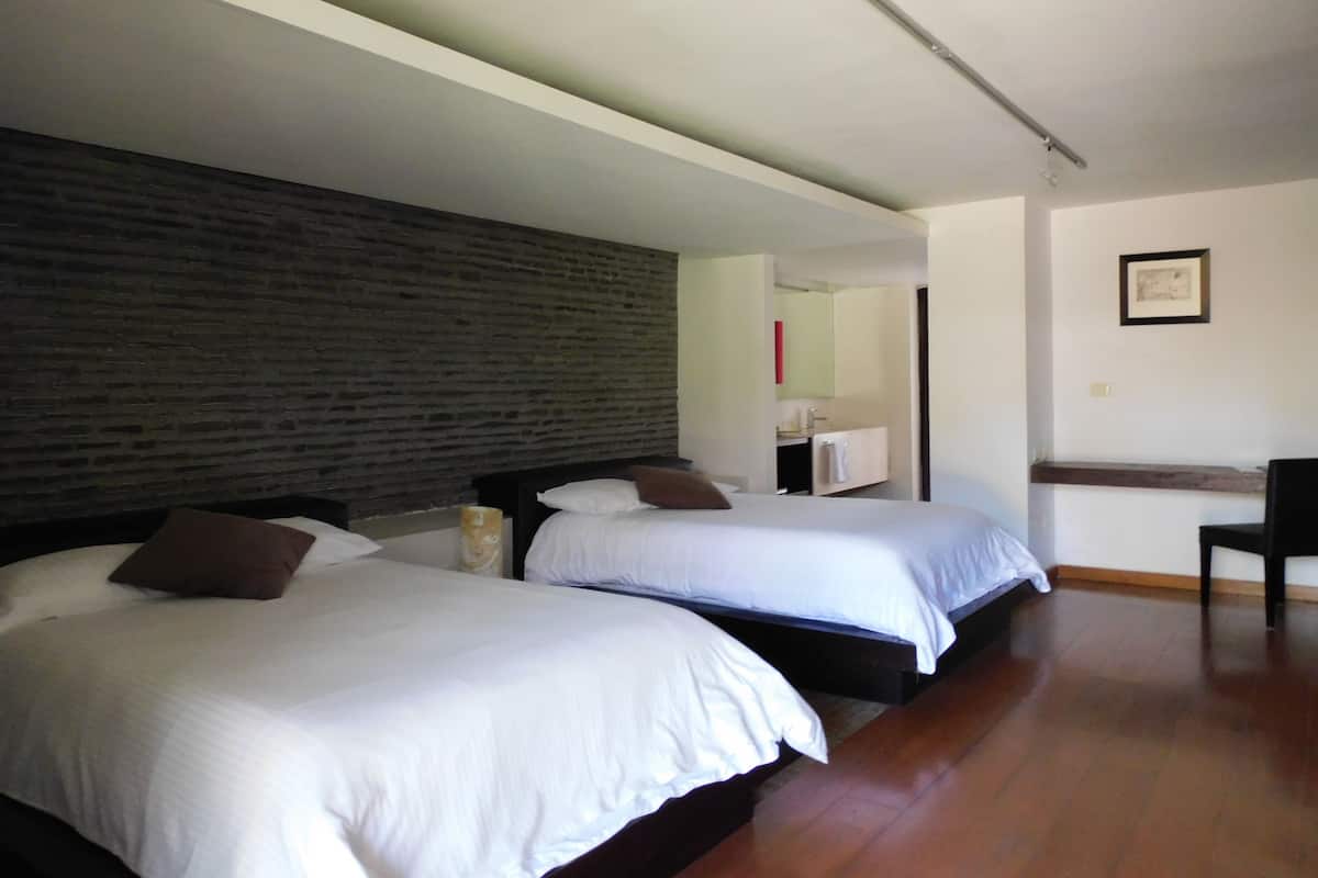 A hotel room with two beds, a brick wall, a mirror, a small desk, and a chair.