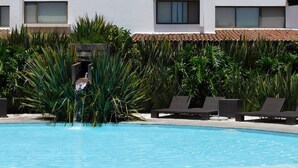 A swimming pool with lounge chairs and a water feature, surrounded by tall plants and a white building with windows. - Hotel & Spa Luna Canela Boutique (Atlixco)