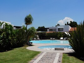 Una piscina con sillones de descanso, rodeada de vegetación y edificios modernos.