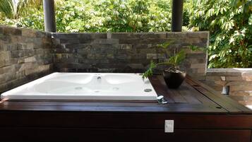 Un jacuzzi bajo una pérgola de madera, con paredes de piedra y abundante vegetación al fondo.