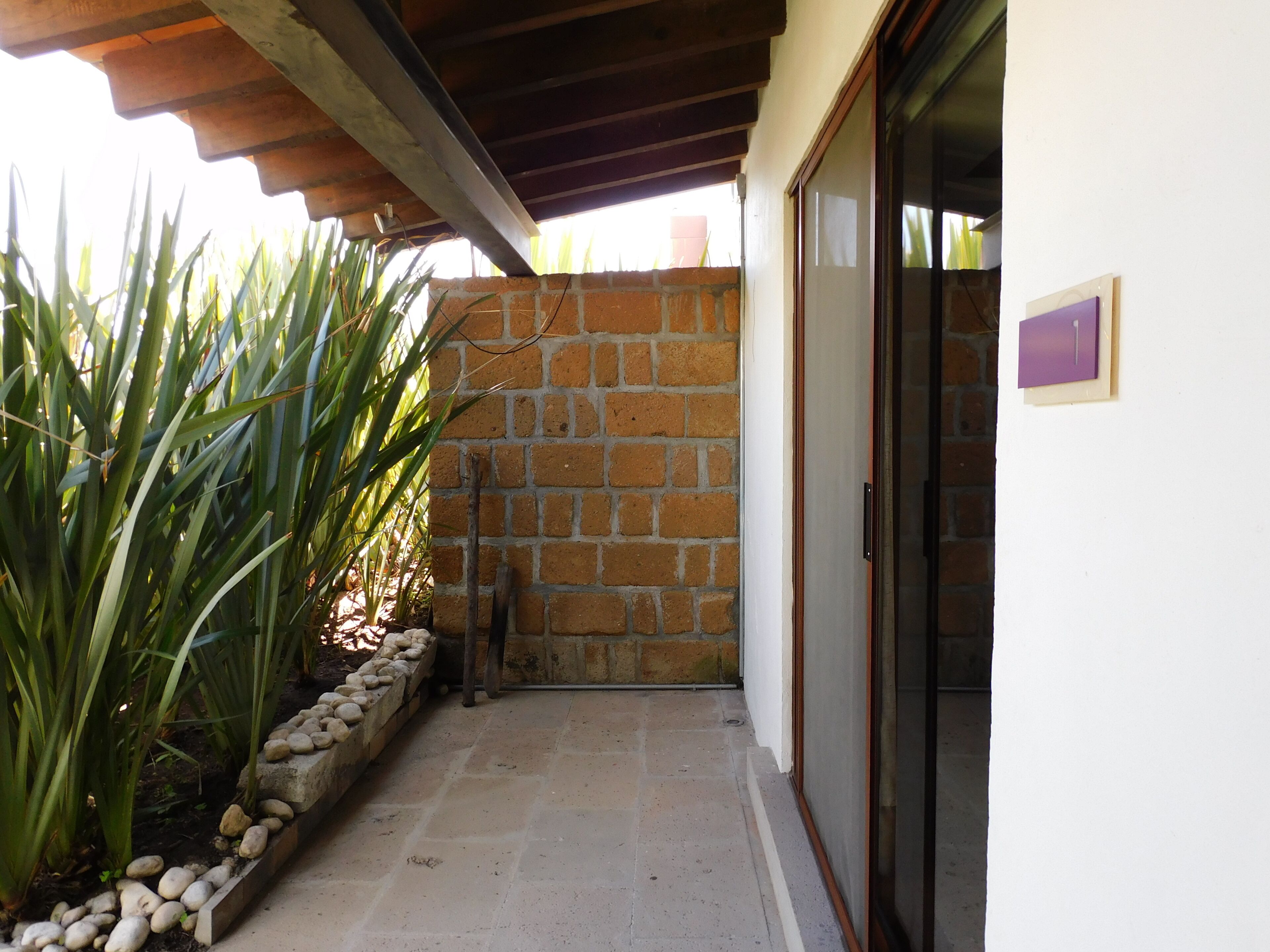 A covered outdoor area with a stone wall, a tiled floor, and a door with a purple sign.
