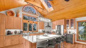 A spacious kitchen with wooden cabinets, a large island with bar stools, a stone backsplash, and a skylight.