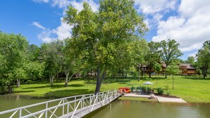 A bridge over a pond with a lawn and a building in the background. - Kentucky Deer Run- Wheelchair Accessible, Lakefront, Private Dock, Fully Updated (Benton)