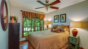 A bedroom with a large bed, a ceiling fan, a window with curtains, a nightstand with a lamp, and a dresser. - Kentucky Deer Run- Wheelchair Accessible, Lakefront, Private Dock, Fully Updated (Benton)