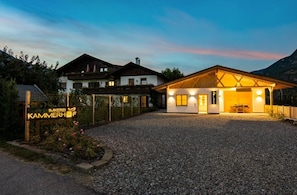 A hotel with a gravel driveway, a sign reading 'IMKEREI KAMMERHOF,' and a building with a wooden facade and a covered outdoor area.