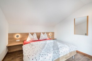 A bedroom with a wooden headboard, a bed with floral bedding, bedside lamps, and a mirror on the wall.