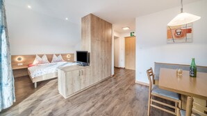 Een slaapkamer met een bed, televisie, houten garderobe en een eethoek met een tafel en stoelen.