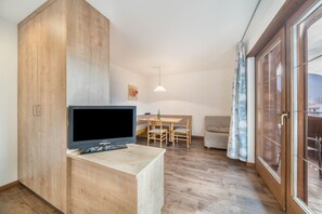 A modern living room with a flat-screen TV, wooden furniture, a dining area, and a large sliding glass door.