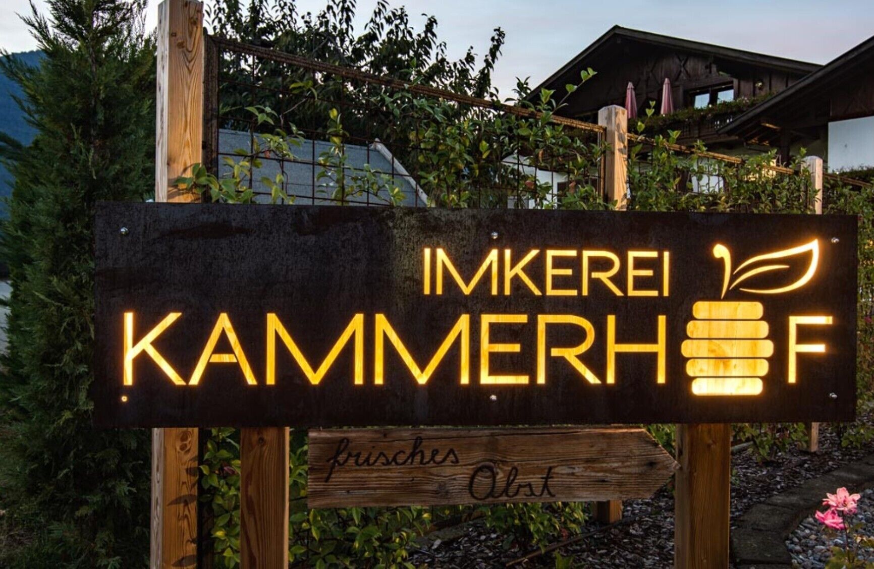 A wooden sign with illuminated text and a honeycomb graphic, indicating a honey shop or brand.