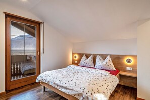 A bedroom with a bed, wooden headboard, bedside tables, and a large window with a view.
