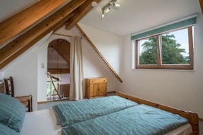 A bedroom with a sloped ceiling, a wooden bed frame, a window with a view of trees, and a small wooden cabinet. - Cozy Apartment “Konrad Schielin” with Mountain View, Wi-Fi & Balcony (Lindau)