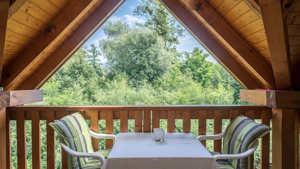 Un terrazzo in legno con tavolo e sedie, vista su alberi e cielo sereno.
