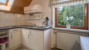 Cucina con mobili bianchi, un piano di lavoro nero, una finestra vista alberi e un lucernario.