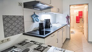 Una cucina compatta con fornello, macchina del caffè e un piccolo piano di lavoro. Presente un rivestimento a parete decorato e un pavimento piastrellato.
