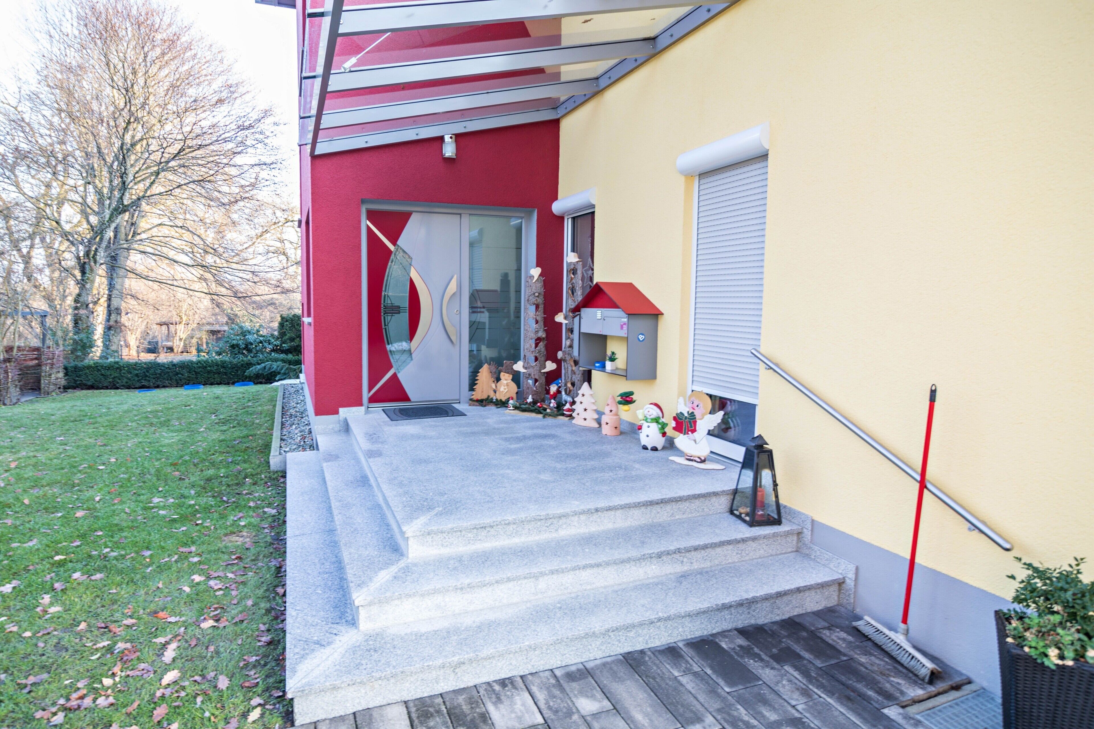 Ein Gebäude mit roter Außenfassade, einer Glastür und einer Treppe, die zu einem kleinen, mit einem roten Dach versehenen Vorbereich führt.