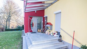 Un edificio con facciata rossa, una porta in vetro e una serie di gradini che conducono a un piccolo portico con tetto rosso.