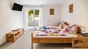 Una camera da letto con un letto, un comodino in legno, una TV montata a parete e una porta scorrevole in vetro che dà su una zona esterna.